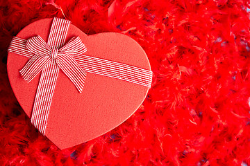 Image showing Heart shaped boxed gift, placed on red feathers background