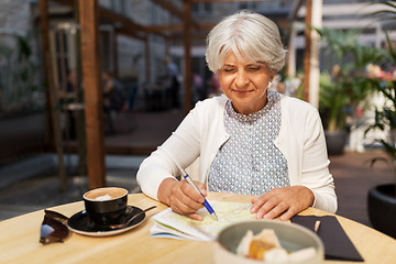 Image showing senior woman with map and coffee at street cafe