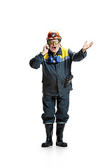 Image showing The studio shot of surprised senior bearded male miner standing at the camera with smartphone on a white background.