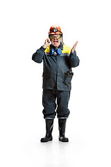 Image showing The studio shot of angry senior bearded male miner standing at the camera with smartphone on a white background.