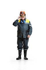 Image showing The studio shot of angry senior bearded male miner standing at the camera with smartphone on a white background.