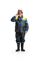 Image showing The studio shot of happy senior bearded male miner standing at the camera with smartphone on a white background.