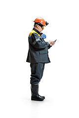 Image showing The studio shot of serious senior bearded male miner standing at the camera with smartphone on a white background.