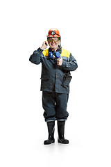 Image showing The studio shot of happy senior bearded male miner standing at the camera with smartphone on a white background.