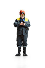 Image showing The studio shot of serious senior bearded male miner standing at the camera with smartphone on a white background.