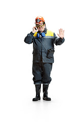 Image showing The studio shot of disgusted senior bearded male miner standing at the camera with smartphone on a white background.