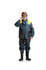 Image showing The studio shot of serious senior bearded male miner standing at the camera with smartphone on a white background.