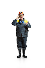 Image showing The studio shot of happy senior bearded male miner standing at the camera with smartphone on a white background.