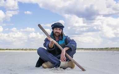 Image showing Man In The Ethnic Clothes Shows A Sand By Hand Sitting In A Dese