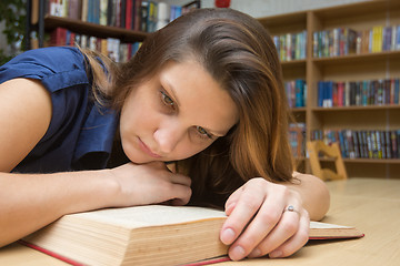 Image showing Tired girl reading a book at the table in the library