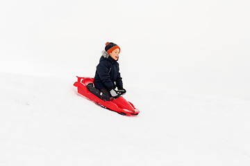 Image showing happy boy sliding on sled down snow hill in winter