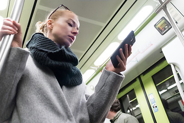 Image showing Beautiful blonde woman wearing winter coat and scarf reading on the phone while traveling by metro public transport.