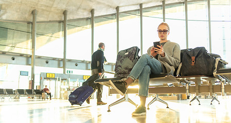 Image showing Female traveler using her cell phone while waiting to board a plane at departure gates at airport terminal.