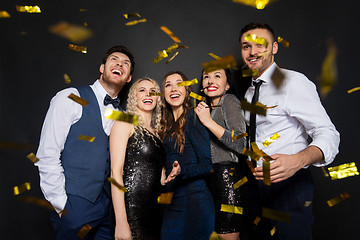 Image showing happy friends at party under confetti over black