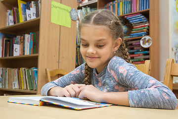 Image showing A girl with a smile reads a book in the reading room