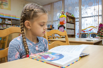 Image showing A girl of ten years old is reading a book in the library