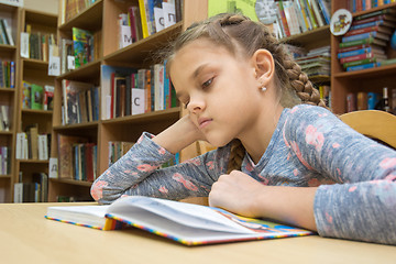 Image showing A girl of ten years old is reading a book in the reading room