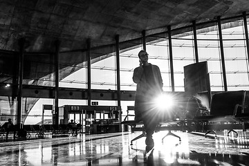 Image showing Female traveler talking on her cell phone while waiting to board a plane at departure gates at airport terminal.