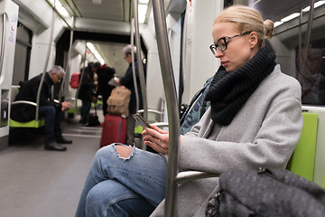 Image showing Beautiful blonde woman wearing winter coat and scarf reading on the phone while traveling by metro public transport.