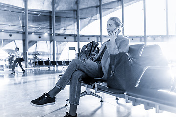 Image showing Female traveler talking on her cell phone while waiting to board a plane at departure gates at airport terminal.