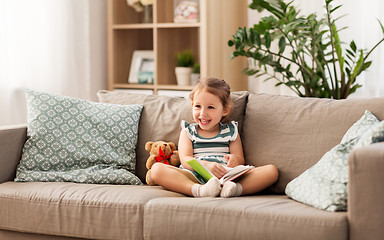 Image showing happy girl sitting on sofa with book at home