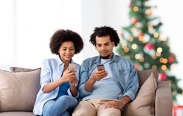 Image showing happy couple with smartphones at home on christmas