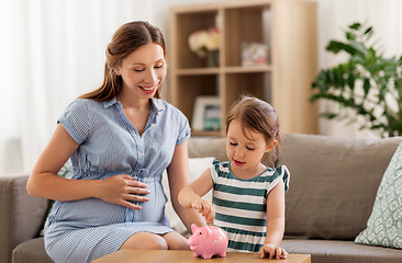 Image showing pregnant mother and daughter with piggy bank