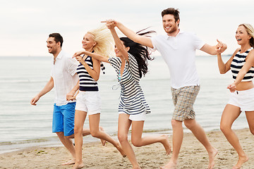 Image showing friends in striped clothes running along beach
