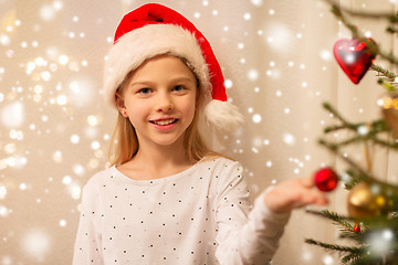 Image showing happy girl in santa hat decorating christmas tree