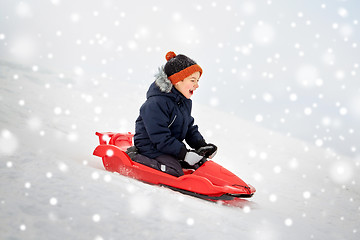 Image showing happy boy sliding on sled down snow hill in winter