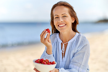 Image showing happy woman eating strawberries on summer beach