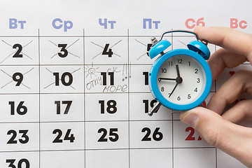 Image showing A hand holds a small alarm clock, in the background is a calendar with the day marked and the word vacation