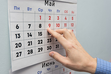 Image showing Office worker\'s hand indicates May holidays on a wall calendar sheet