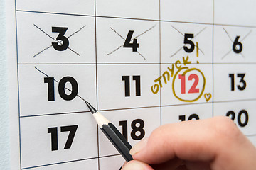 Image showing A hand crosses out the penultimate day before the holiday with a pencil in the calendar