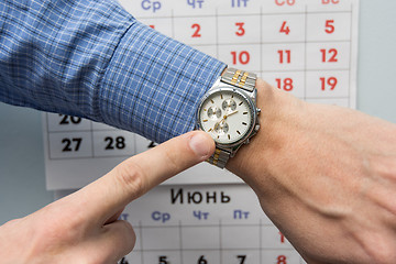 Image showing Office specialist\'s hand points to a wristwatch, in the background is a wall calendar