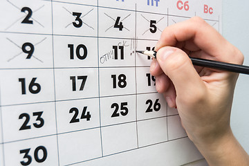 Image showing The hand with a pencil writes the word vacation in the wall calendar