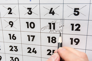 Image showing The hand with a pencil writes the words vacation and sea on a wall calendar