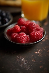 Image showing Close up on fresh raspberries placed on ceramic saucer on dark rusty table.