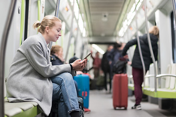 Image showing Beautiful blonde woman wearing winter coat reading on the phone while traveling by metro public transport.