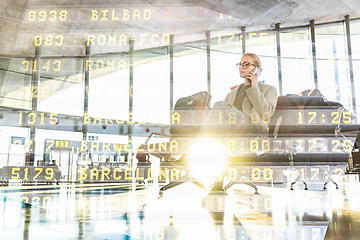 Image showing Female traveler talking on her cell phone while waiting to board a plane at departure gates at airport terminal.