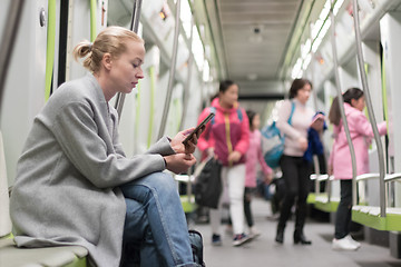 Image showing Beautiful blonde woman using smart phone while traveling by metro public transport.