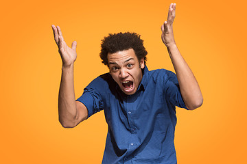 Image showing The young emotional angry man screaming on orange studio background