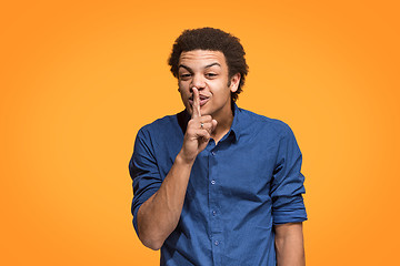 Image showing The young man whispering a secret behind her hand over orange background