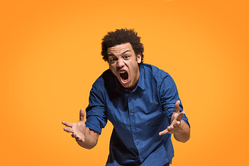 Image showing The young emotional angry man screaming on orange studio background