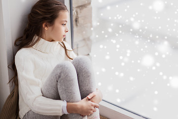 Image showing sad girl sitting on sill at home window in winter