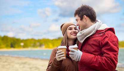 Image showing happy couple with coffee cups over autumn beach