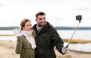 Image showing happy couple taking selfie on beach in autumn