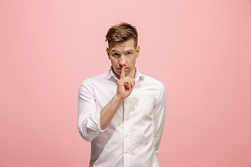 Image showing The young man whispering a secret behind her hand over pink background