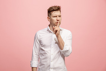 Image showing The young man whispering a secret behind her hand over pink background