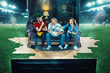 Image showing Ardent fans are sitting on the sofa and watching TV in the middle of a football field.